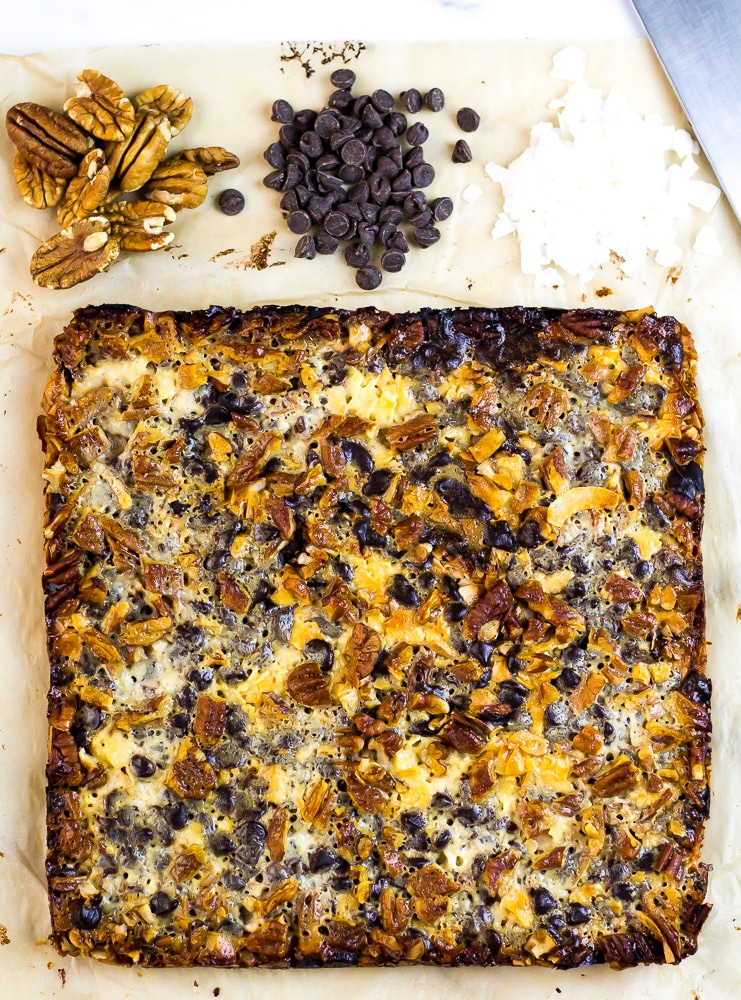 Keto Magic Bars on cutting board with chocolate chips, pecans and coconut